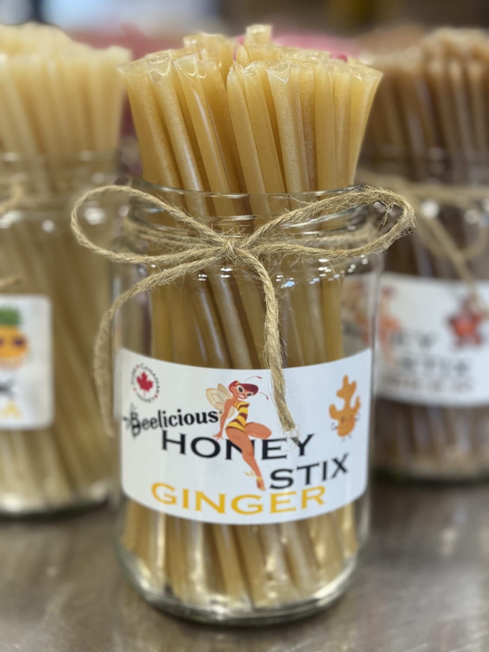 A jar of honey ginger sticks tied with twine, labeled "Delicious Honey Ginger Stix."