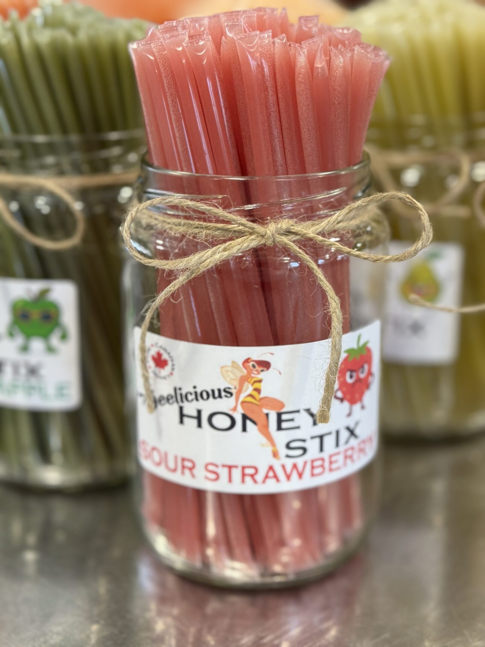 Jar of pink strawberry-flavored honey sticks tied with twine.