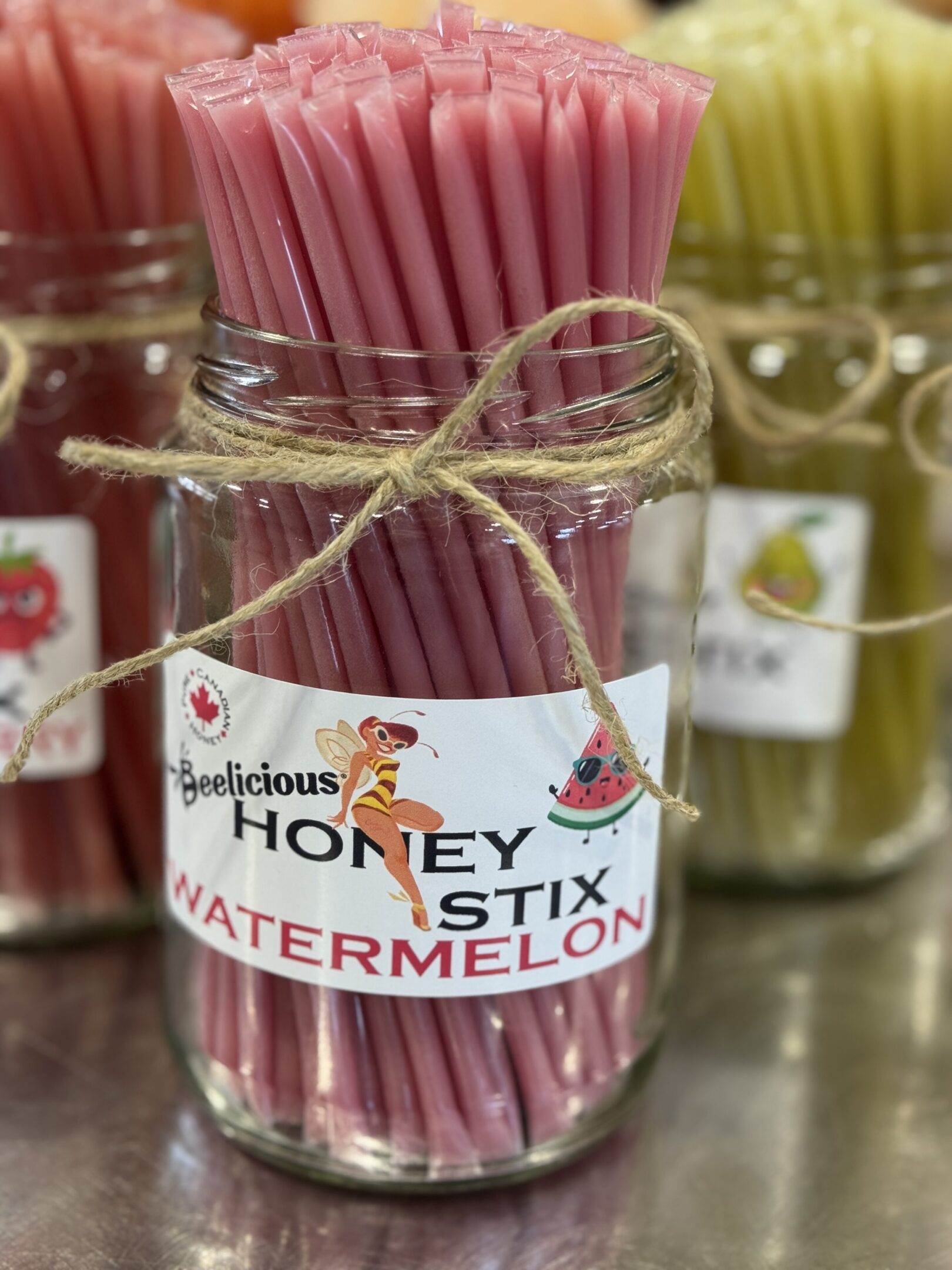 Jars of colorful honey stick watermelon candy tied with rustic string.
